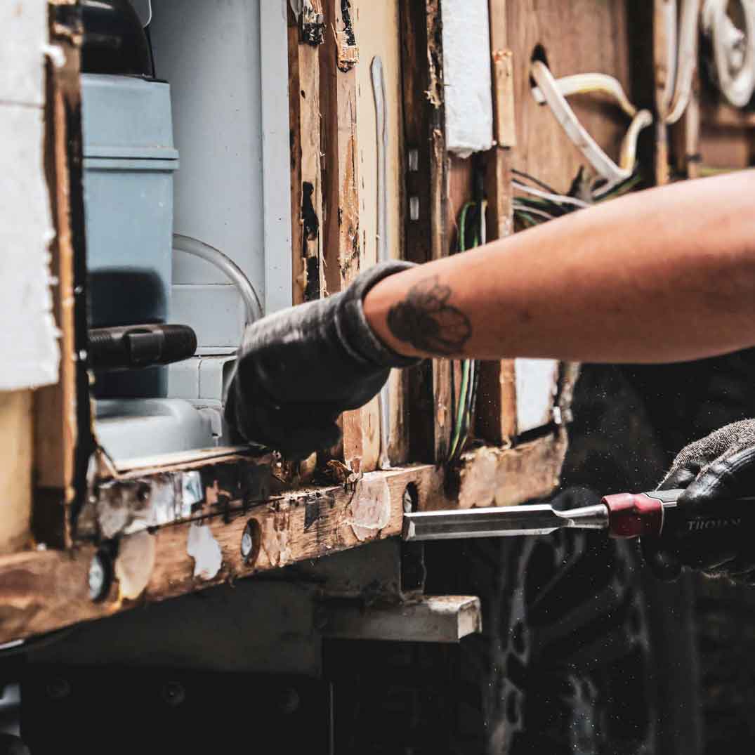caravan repair technician using a chisel to remove rotted timber from caravan frame